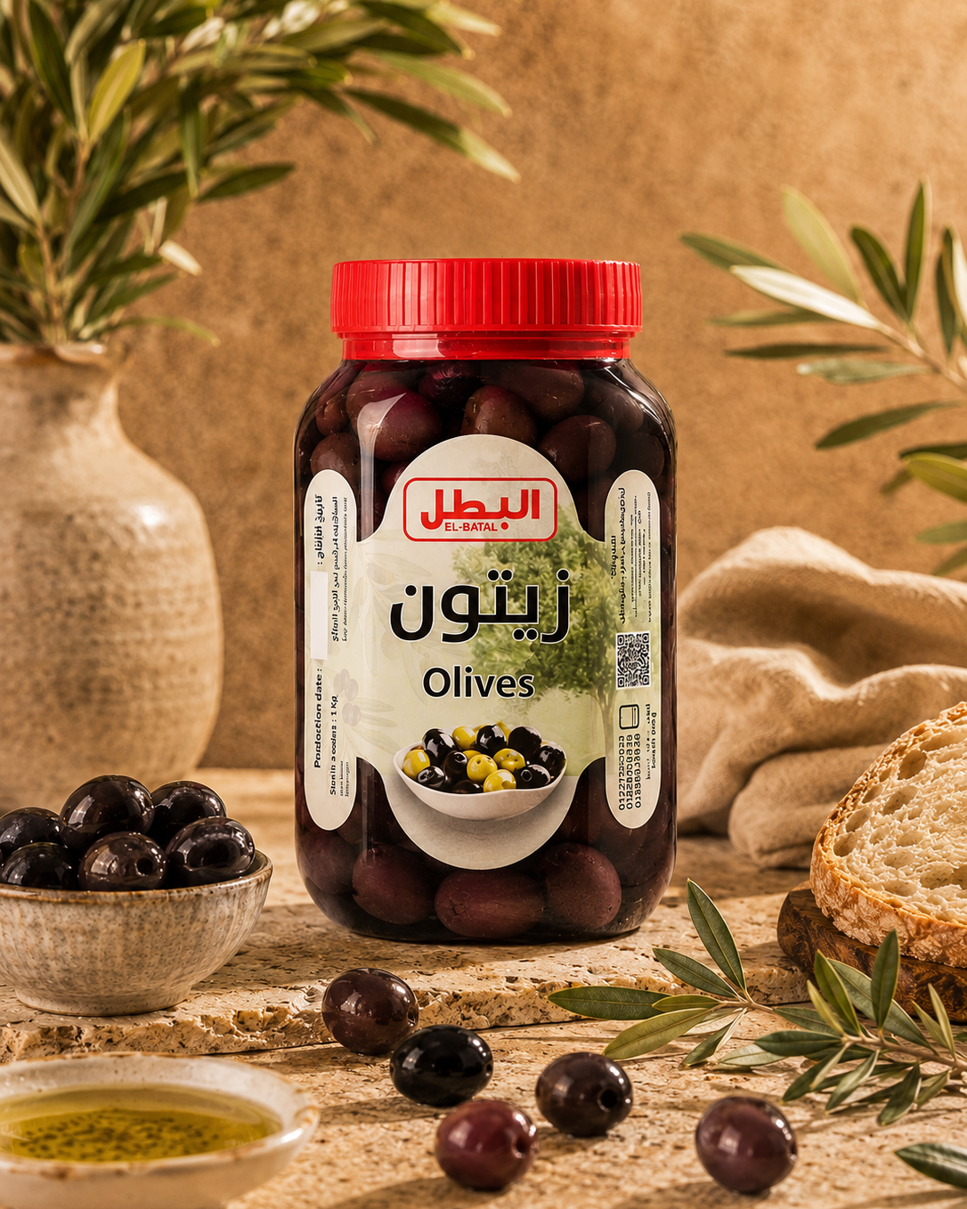A jar of El Ghalil brand black olives with a red lid and a white label, styled on a rustic stone surface with olive branches, bread, and a bowl of olives.